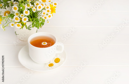 Fototapeta Naklejka Na Ścianę i Meble -  Chamomile tea in a white cup on a white wooden background with a bouquet of daisies with copy space.