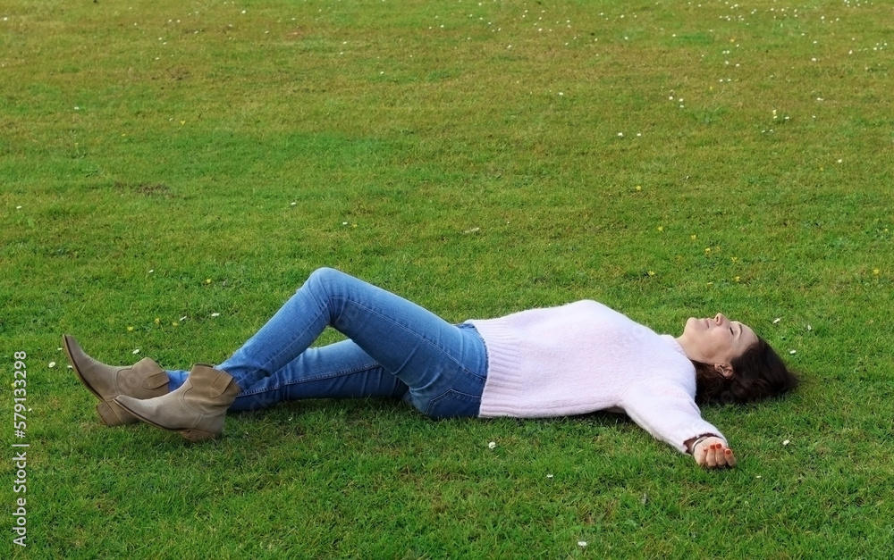 Caucasian woman lies on the green grass on a spring day. Concept of a happy life, de-stressing. Tranquility on vacation. Caucasian woman lies on the green grass on a spring day. Concept of a happy life, de-stressing. Tranquility on vacation.