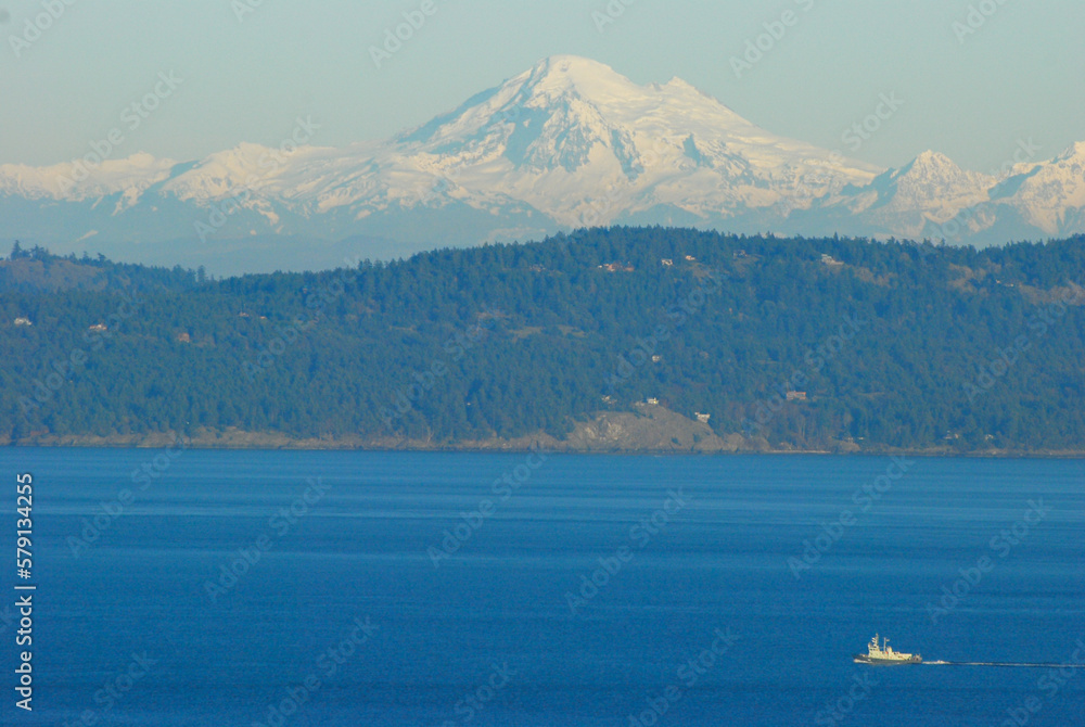 A tugboat motors in front of snow covered Mount Baker on a calm and sunny winters day