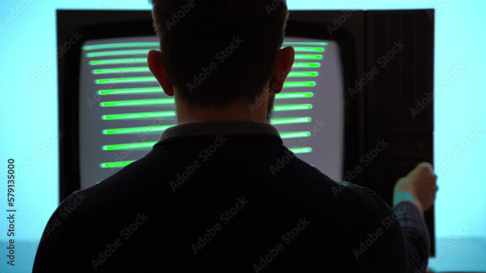 Man sitting in front of retro TV with green screen blinking monitor and horizontal stripes, person changing channels on control panel searching for good TV signal. Vintage television on turquoise Man sitting in front of retro TV with green screen blinking monitor and horizontal stripes, person changing channels on control panel searching for good TV signal. Vintage television on turquoise