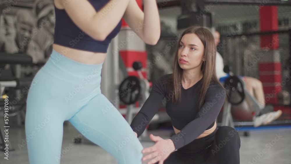Female personal trainer corrects and advises her brunette client during training in the gym. Female personal trainer corrects and advises her brunette client during training in the gym.