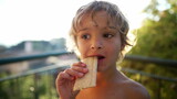 Portrait of a child eating cookie cracker outdoors in sunlight. Close up of male kid face outdoors. Blond small boy