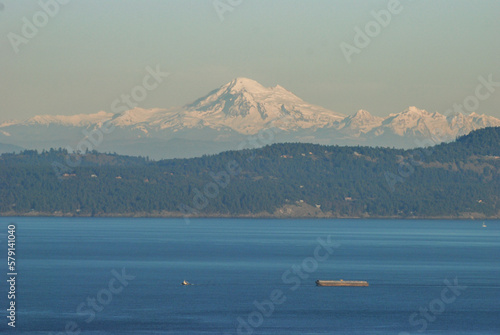 A tugboat and barge navigate a passage at the south end of Vancouver Island. In the distance we see the beautiful Mount Baker standing tall