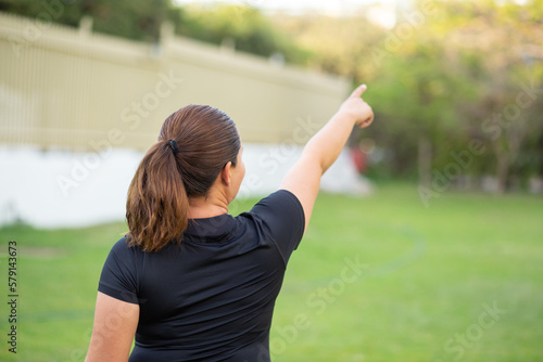 Sport woman doing exercise in a park with black clothes pointing to the air