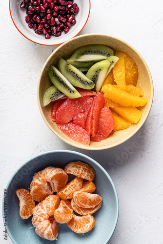 Bowls with fresh fruits (grapefruits,  tangerines, pomegranate seeds, oranges, and kiwi), preparing fruit salad, ingredients