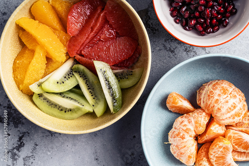 Bowls with fresh fruits (grapefruits,  tangerines, pomegranate seeds, oranges, and kiwi), preparing fruit salad, ingredients