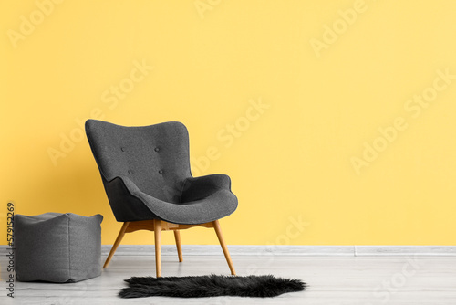 Fototapeta Naklejka Na Ścianę i Meble -  Stylish grey armchair, pouf and black fur rug near yellow wall