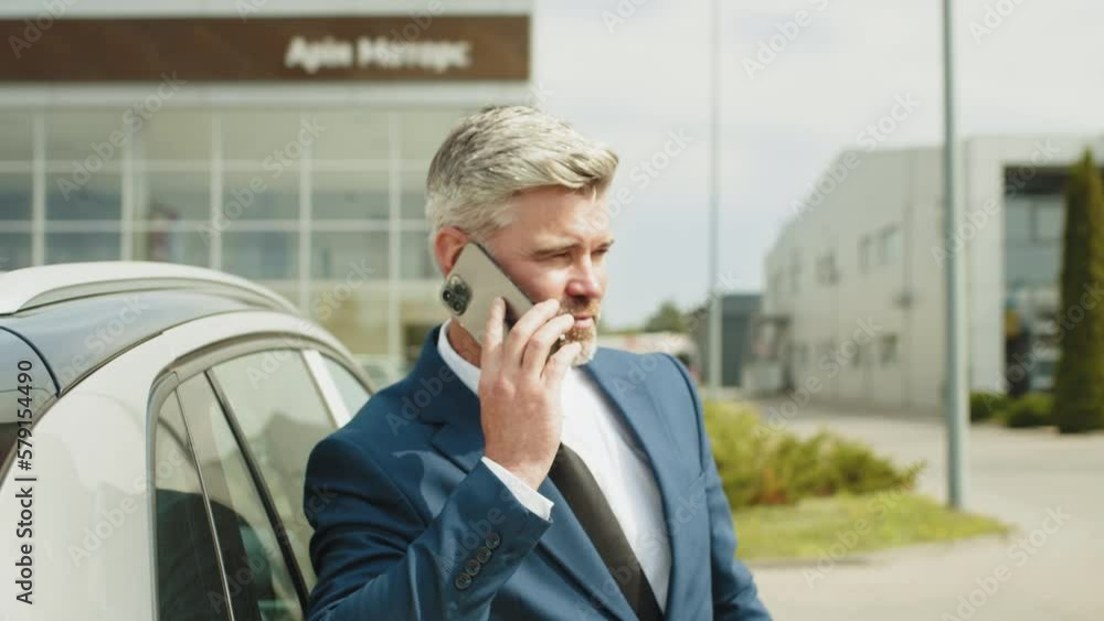 Handsome man talking on phone while electric car charging, closeup. Businessman charging electric car at outdoor charging station, man unplugging electric car from charging station Handsome man talking on phone while electric car charging, closeup. Businessman charging electric car at outdoor charging station, man unplugging electric car from charging station