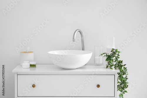 Sink with bath accessories  candles and houseplant on chest of drawers near light wall