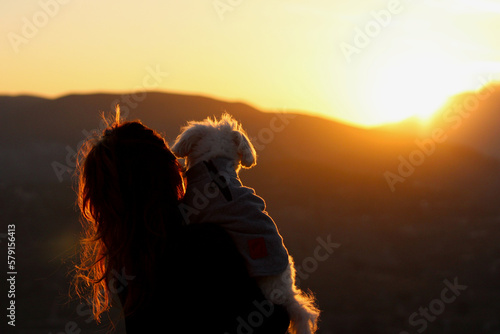 mujer observando el amanecer con su bichón maltés