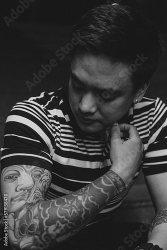 Black and White portrait of an asian man looking at his tattoo - Asian man having tattoos in his right arm - Closeup portrait of man having tattoos © Abhinav Joshi