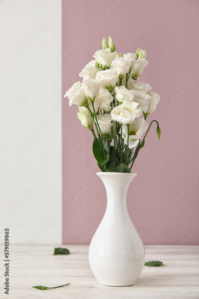 Vase with delicate eustoma flowers on table near color wall Vase with delicate eustoma flowers on table near color wall