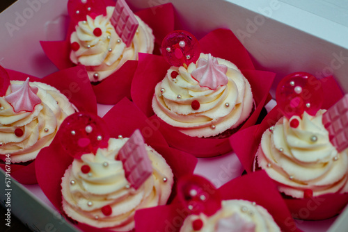 Six birthday cupcakes in a box. Cute decoration. White pies with curd cream, pink chocolate and lollipops. For a girls party.