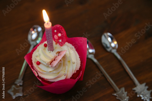 Tasty cupcake for birthday party with candel and spoons on a brown wooden table. Cakes decorated with white cheese cream, pink lollipop and chocolate. For a girls party.