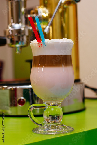 Coffee cocktail with foam and coconut flakes with two straws. Coffee machine on background.