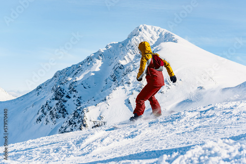 Unrecognizable person descending a ski slope on a snowboard with an impressive snowy mountain in the background. mountain and winter sport