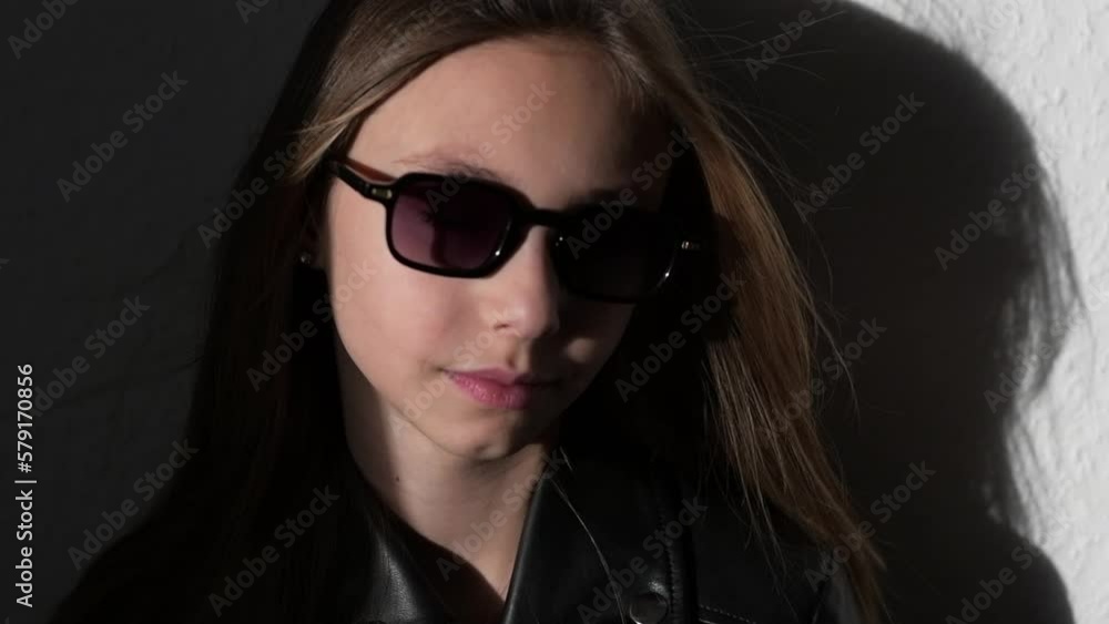 Slow motion video of a stylish child in leather jacke with glasses , the wind blows in her face and inflates the hair