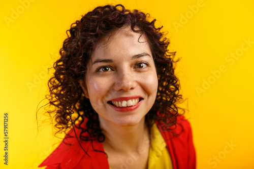 Studio shot of positive and the smiling pretty female. Curly girl in bright red shirt and yellow t-shirt. Isolated on yellow background. Close up.