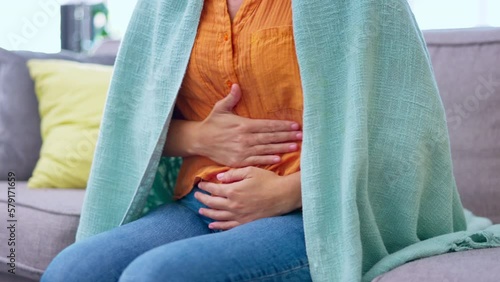 Hands, stomach pain and woman on sofa in house living room with menstrual cramps or period. Sick, health and young female suffering with painful endometriosis, abdominal problem or constipation. photo