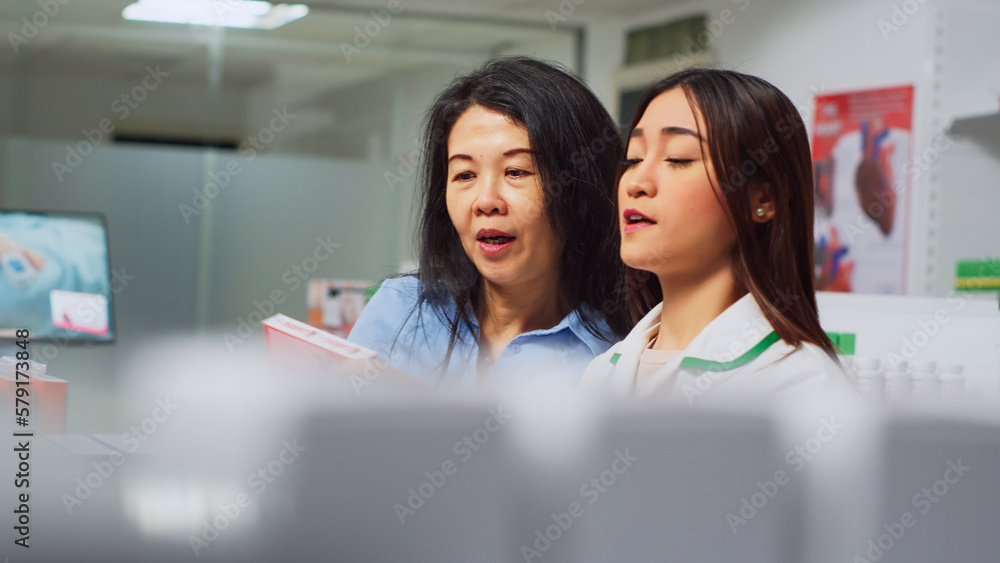 Asian woman showing prescription paper to pharmacist, asking for help in finding medicaments. Female client looking for medicine and boxes of pills, talking to health specialist. Handheld shot.
