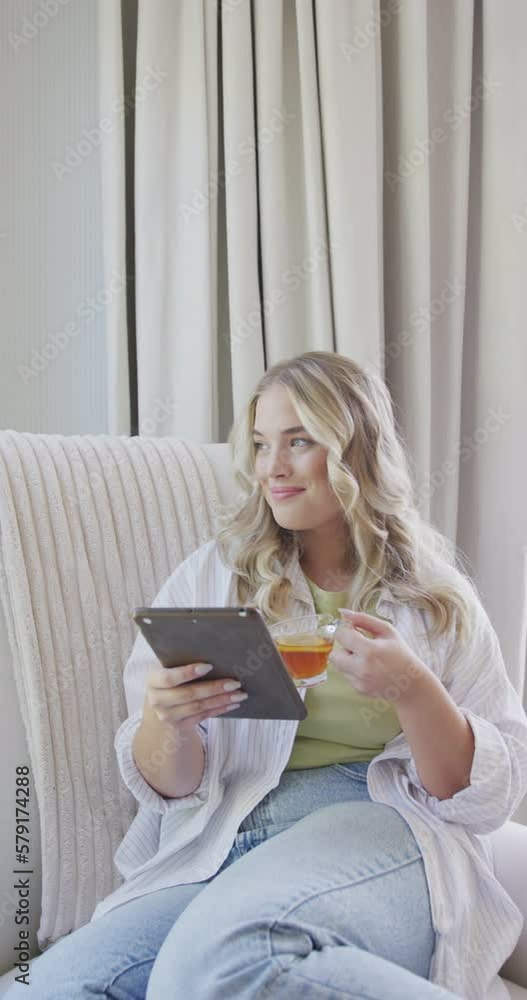 Vertical video of happy caucasian plus size woman with tea using tablet in slow motion Vertical video of happy caucasian plus size woman with tea using tablet in slow motion