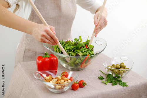 close-up of salad kneading with wooden spoons cherry tomatoes cocktail cucumbers olives and other ingredients lie on table with beige tablecloth beige apron restaurant food serving table setting