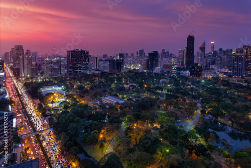 Elevated, panoramic view over the popular Lumphini Park to the illuminated city skyline and the busy Rama IV Road of Bangkok, Thailand, during a colorful sunset