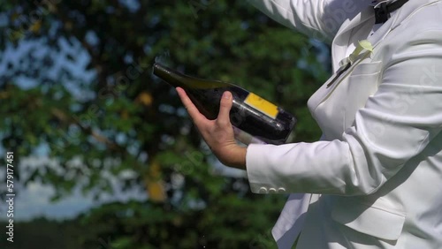 Sabrage. Man in white suit opens bottle of champagne or wine with knife or saber. Groom in jacket in wedding day, unrecognizable person. Waiter performance at the party sabering.
