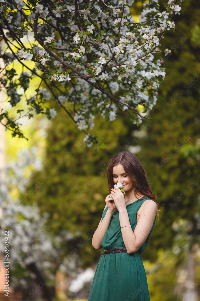 Woman-spring. Young woman in long green dress in a blooming apple garden. Spring story. Brown-haired girl with long hairs. Woman-spring. Young woman in long green dress in a blooming apple garden. Spring story. Brown-haired girl with long hairs.