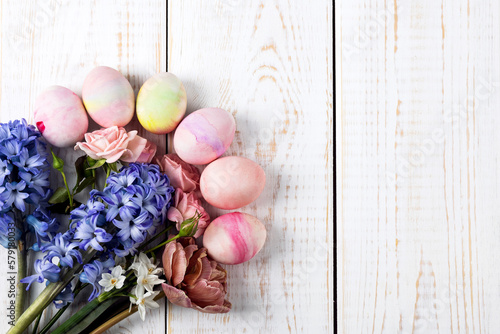 Spring bouquet of daffodils, hyacinths, roses, tulips with colorful easter eggs on a white wooden background. Happy Easter concept. Greeting card, copy space