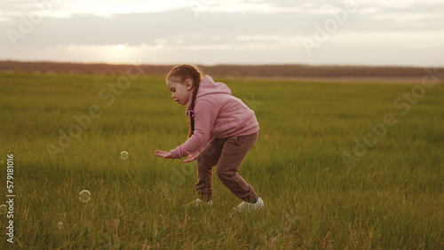 happy child playing park with soap bubbles sunset. cheerful girl run green lawn playing with soap bubbles forest. emotions child girl playing with festive soap balls. positive mood kid park. family.