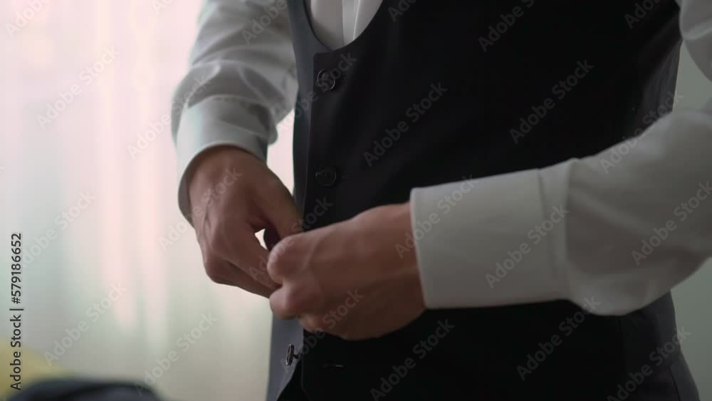 A man is fastening a button on a black jacket or vest. Male wears a classic suit. Businessman, office worker or groom. A man is fastening a button on a black jacket or vest. Male wears a classic suit. Businessman, office worker or groom.