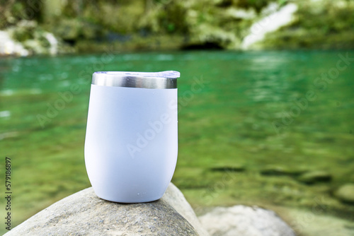 This stunning image captures the beauty of a white wine tumbler, carefully placed near the peaceful flow of a nearby river