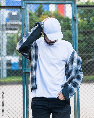 With his rugged good looks and sharp sense of style, this bearded man creates a captivating image in a white blank shirt and cap hat © Said