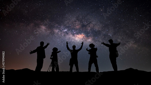 Landscape with colorful Milky Way and yellow light. Night starry sky with silhouette of a sporty happy people with raised-up arms on the rock. Beautiful Universe. Space background