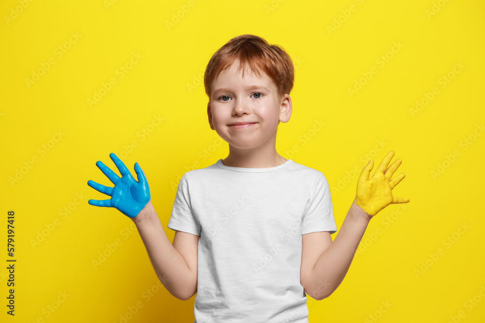Little boy with hands painted in Ukrainian flag colors on yellow background. Love Ukraine concept Little boy with hands painted in Ukrainian flag colors on yellow background. Love Ukraine concept