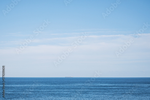 広い空と大きな海、遠くに小さく見える貨物船