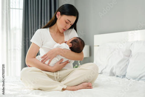 mother holding and consoling her newborn baby to sleeping on bed