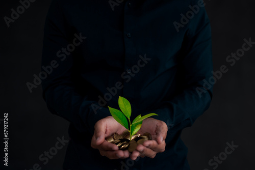 Young businessman holding coins and young plant and seeding nurture grow environmental and reduce global warming help earth, ecology agriculture concept.