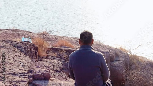 isolated man sitting at mountain top with lake view from flat angle video is taken at kaylana lake jodhpur rajasthan india. photo