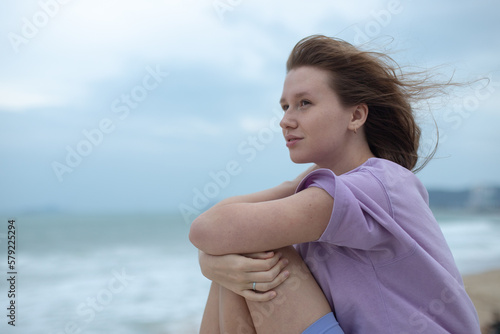 Stampa su tela Young calm sad serious woman is sitting on embankment near sea, ocean on beach,