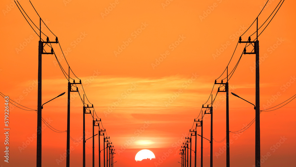 Silhouette rows of many electric power poles with cable lines against beautiful orange sunset sky background in perspective view