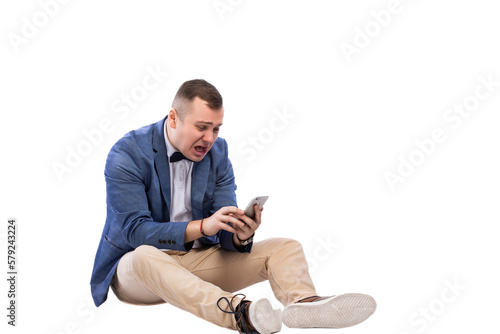 Shocked young guy looking into a smartphone while sitting on the floor on a white background © zamuruev