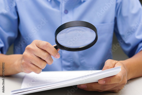 Close up hand of businessperson looking at documents through magnifying glass. Concept of business and data validation.