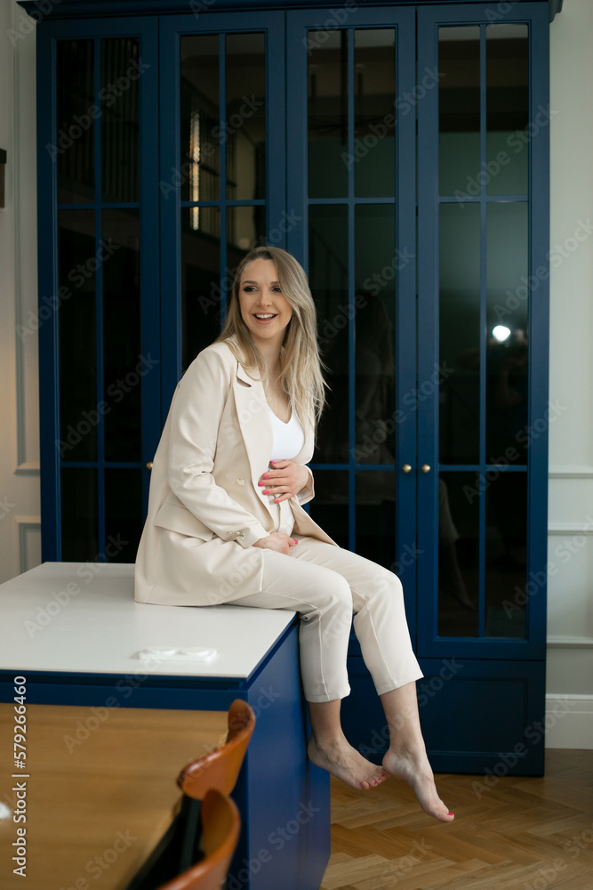 Happy charming pregnant businesswoman sits at home against background of blue doors and gently hugs her stomach. Happy charming pregnant businesswoman sits at home against background of blue doors and gently hugs her stomach.