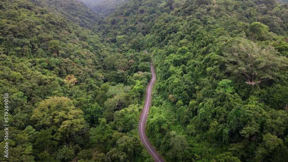 Epic aerial shot of remote road over top of mountain with green jungle in Sumbawa Island, Indonesia. The transportation road across mountain rain forest. Shot from drone. Epic aerial shot of remote road over top of mountain with green jungle in Sumbawa Island, Indonesia. The transportation road across mountain rain forest. Shot from drone.
