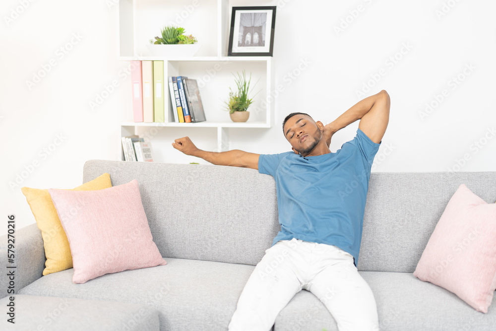 Young man, sitting on the couch stretching his neck after many hours of work. Young man, sitting on the couch stretching his neck after many hours of work.