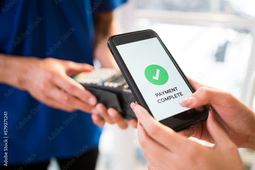 Woman paying bill through smartphone using contactless payment technology. Satisfied customer paying through mobile phone using NFC technology. Closeup hands of mobile payment at mobile handheld POS.