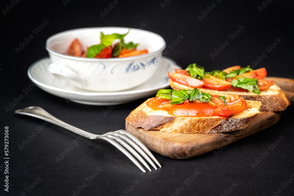 Close up view of tasty bruschettas with cherry tomatoes, basil and olive oil on a wooden board. Italian style cuisine..