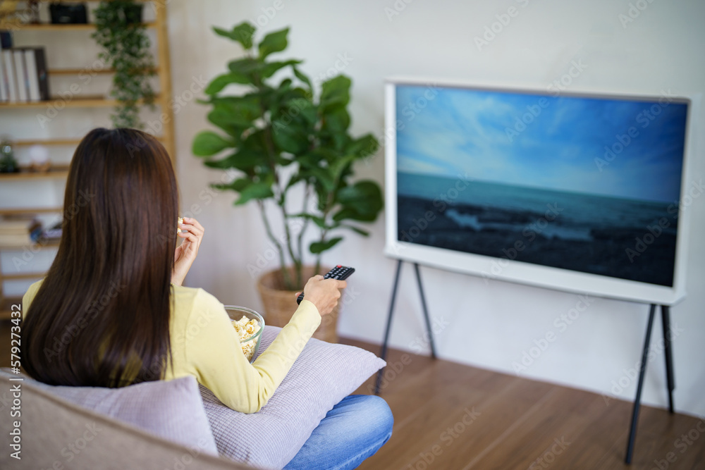 Asian woman Watching smart TV and using remote controller Hand holding television audio remote control at home with the remote control television Asian woman Watching smart TV and using remote controller Hand holding television audio remote control at home with the remote control television
